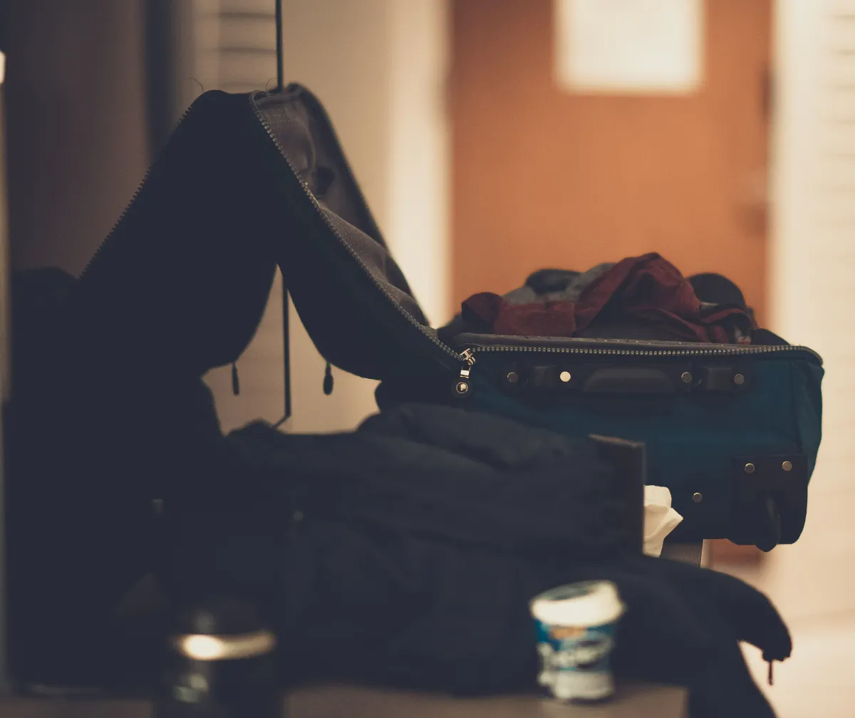 An open suitcase on a bed in a dim room with clothes being folded into it